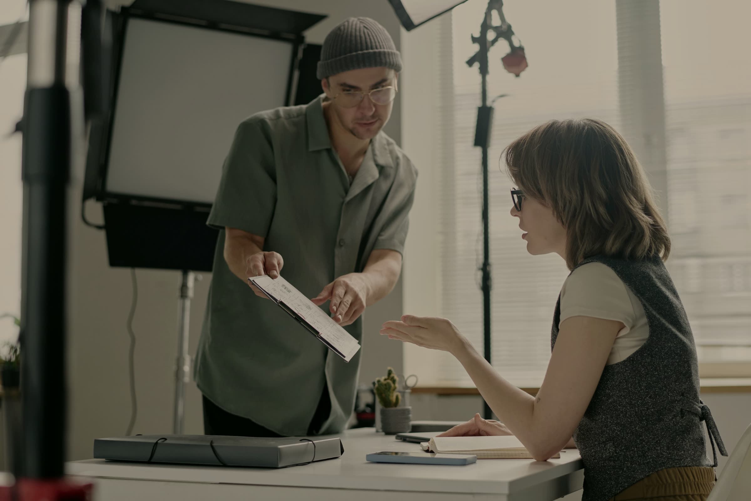 Crew member handing a printed document across a desk to a colleague on a lit studio set