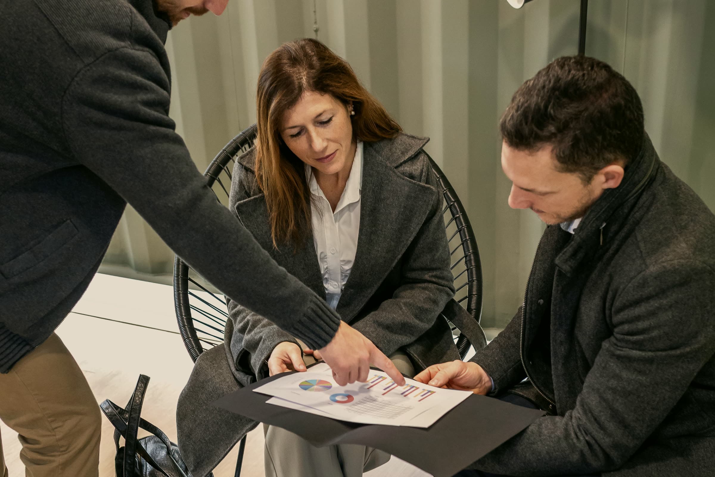 A client and colleague going over a printed document while a third person points to a line on the page