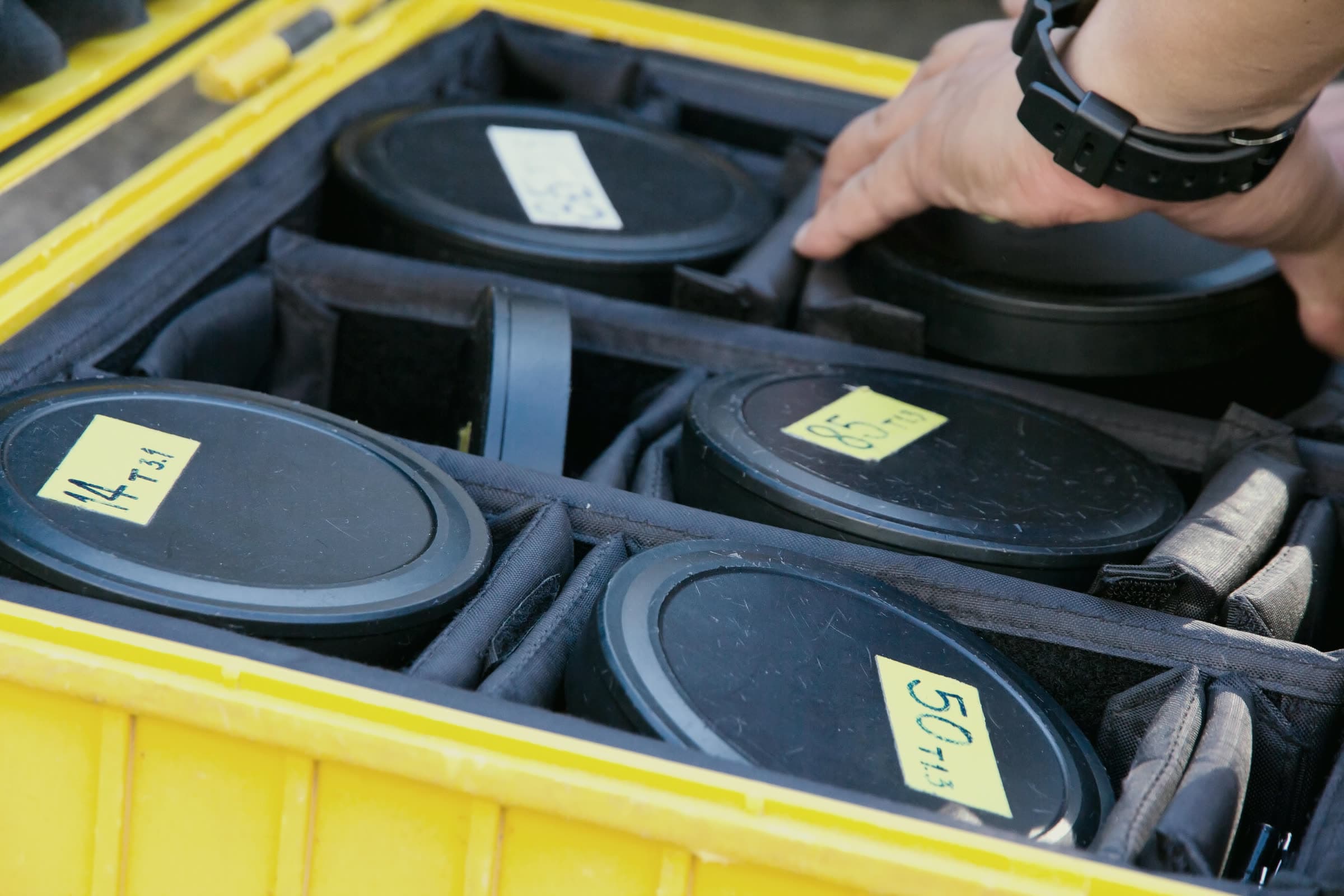 Hand lifting a labeled cinema lens from a foam-lined yellow equipment case
